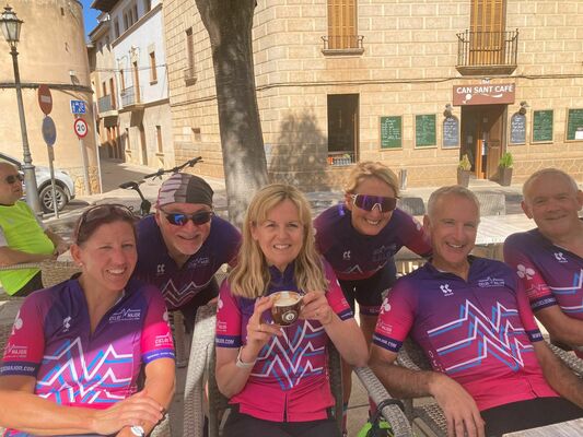 Cyclists sitting in chairs, looking at the camera; one is holding a coffee